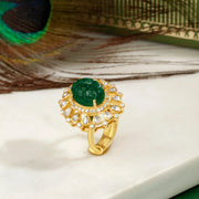 Gold plated silver ring with green gemstone and peacock feather on a white surface